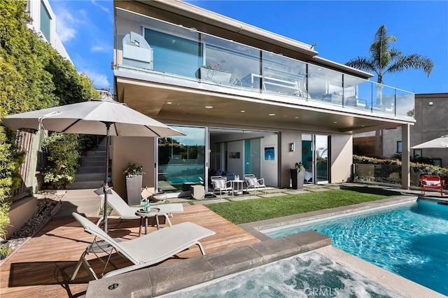 rear view of property featuring a balcony, stairs, an outdoor pool, and stucco siding