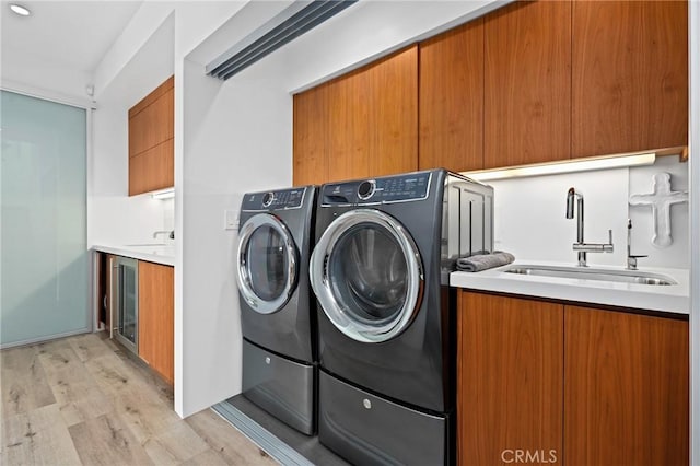 laundry room featuring cabinet space, light wood-style flooring, wine cooler, washer and dryer, and a sink