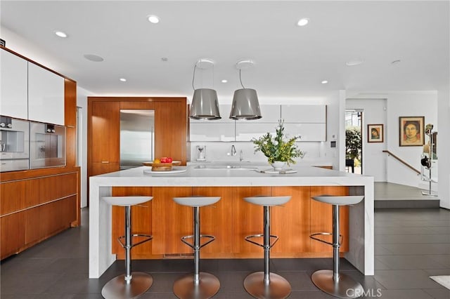 kitchen featuring a breakfast bar, recessed lighting, light countertops, brown cabinetry, and white cabinets