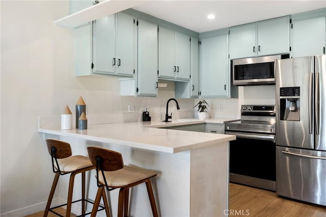 kitchen featuring appliances with stainless steel finishes, a kitchen breakfast bar, a peninsula, light countertops, and a sink