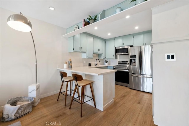 kitchen with light countertops, light wood-style flooring, appliances with stainless steel finishes, a sink, and a peninsula