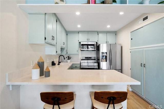 kitchen featuring stainless steel appliances, a breakfast bar, a peninsula, a sink, and light countertops