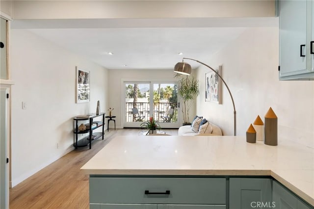 kitchen with light countertops, light wood-type flooring, green cabinetry, a peninsula, and baseboards