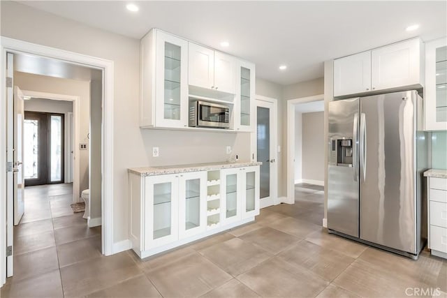 kitchen with light stone counters, recessed lighting, stainless steel appliances, white cabinets, and glass insert cabinets