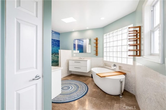 bathroom featuring a freestanding tub, tile walls, a healthy amount of sunlight, and vanity