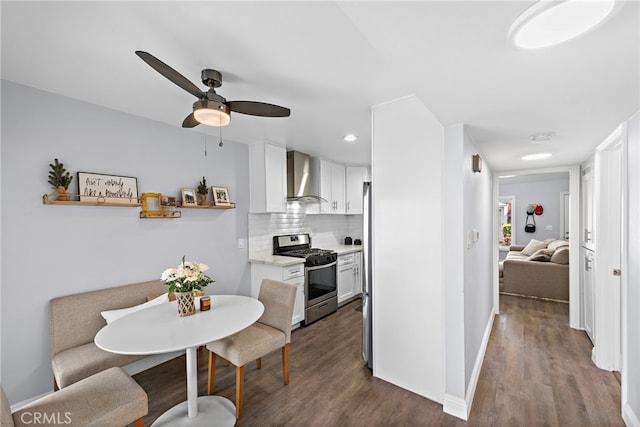 kitchen featuring white cabinets, light countertops, wall chimney range hood, stainless steel gas range, and backsplash