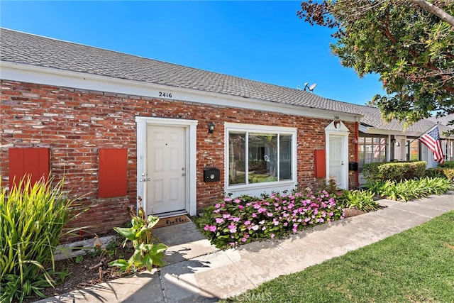 entrance to property featuring brick siding and roof with shingles