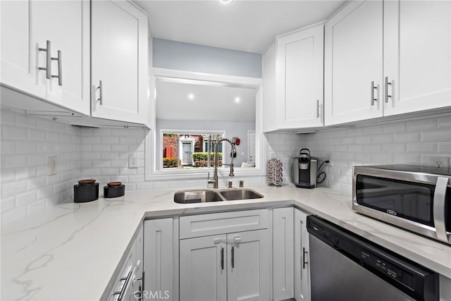 kitchen with appliances with stainless steel finishes, white cabinetry, a sink, and light stone counters