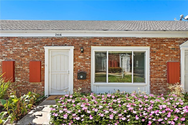 doorway to property featuring a shingled roof and brick siding