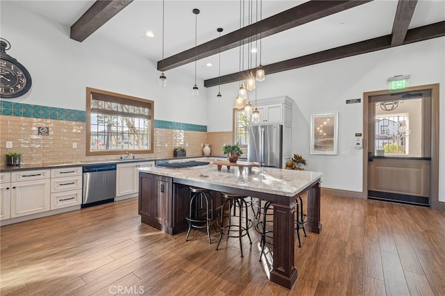 kitchen featuring wood-type flooring, beamed ceiling, a breakfast bar area, and appliances with stainless steel finishes