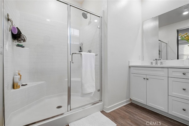 full bath with vanity, baseboards, wood finished floors, and a stall shower
