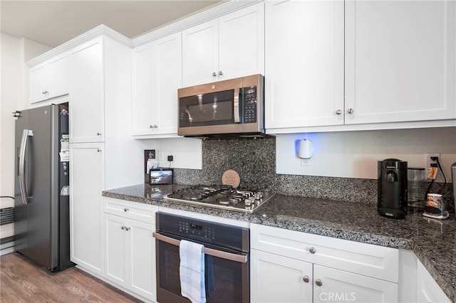 kitchen featuring light wood finished floors, white cabinetry, dark stone counters, and appliances with stainless steel finishes