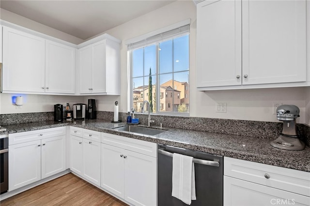 kitchen featuring dark stone countertops, a sink, white cabinetry, light wood-type flooring, and dishwasher
