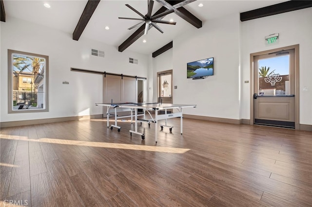 dining space featuring beam ceiling, healthy amount of natural light, wood finished floors, a barn door, and baseboards