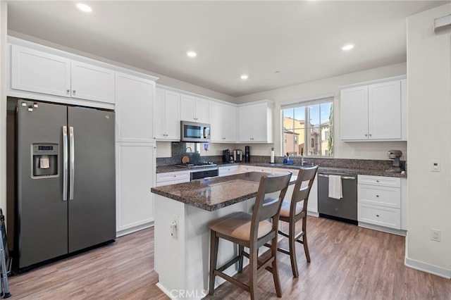 kitchen with white cabinetry, a breakfast bar, light wood finished floors, and appliances with stainless steel finishes