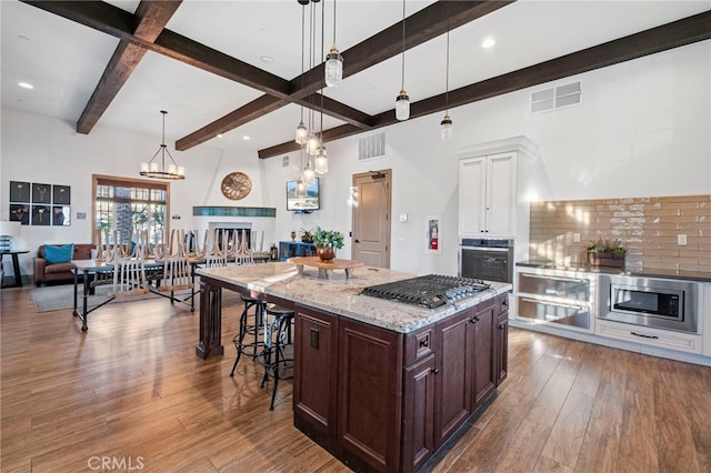 kitchen with appliances with stainless steel finishes, beamed ceiling, white cabinets, hardwood / wood-style flooring, and light stone counters