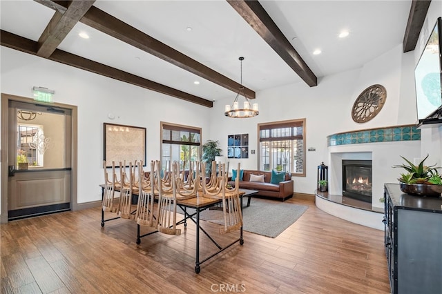 dining space with beamed ceiling, a notable chandelier, a glass covered fireplace, and wood finished floors