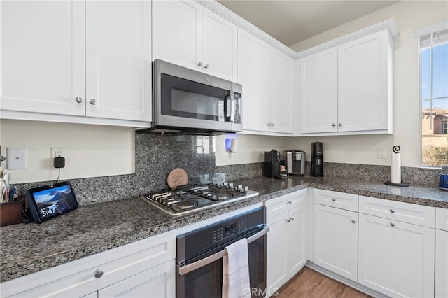 kitchen featuring stainless steel appliances, dark stone counters, light wood-style flooring, white cabinetry, and decorative backsplash