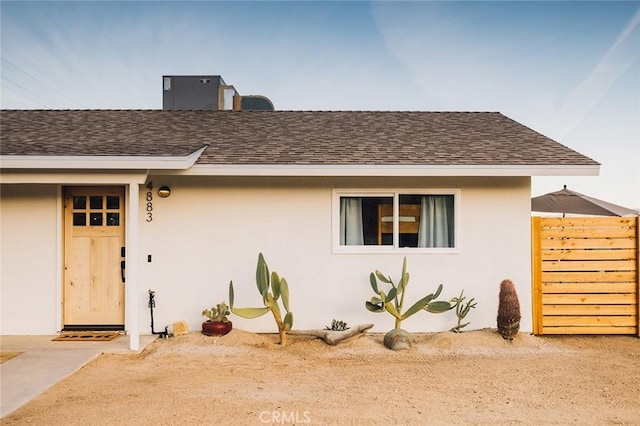 entrance to property with a shingled roof, fence, and stucco siding