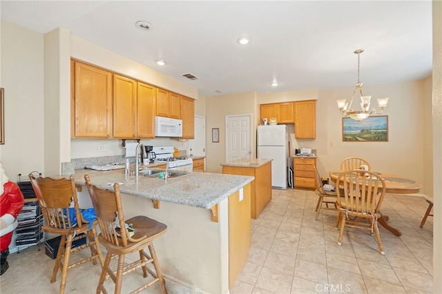 kitchen featuring decorative light fixtures, a sink, light stone countertops, white appliances, and a peninsula