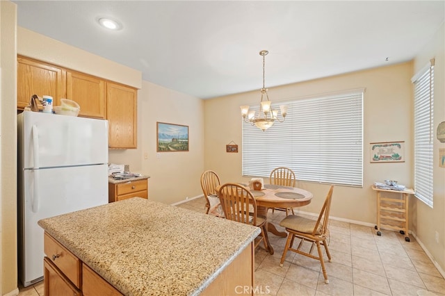 kitchen featuring light stone counters, a center island, freestanding refrigerator, a chandelier, and pendant lighting