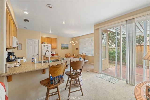 kitchen with white appliances, a sink, visible vents, light stone countertops, and pendant lighting