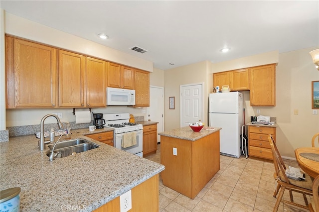 kitchen featuring white appliances, visible vents, light stone counters, a center island, and a sink