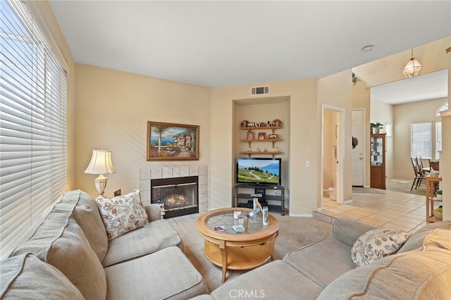 living area with a fireplace, light colored carpet, visible vents, light tile patterned flooring, and baseboards