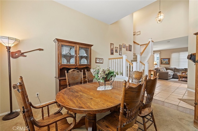 dining space with light tile patterned floors, light carpet, a high ceiling, baseboards, and stairs