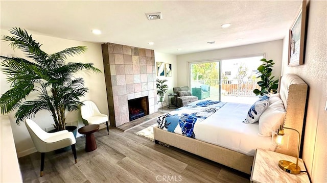 bedroom with a tile fireplace, recessed lighting, visible vents, access to exterior, and light wood finished floors