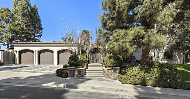 view of front of house with a garage, driveway, a gate, and stucco siding