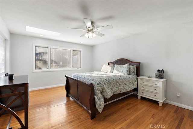 bedroom featuring ceiling fan, baseboards, a skylight, and light wood finished floors