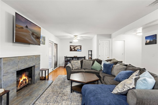 living area with wood finished floors, baseboards, visible vents, ceiling fan, and a tiled fireplace