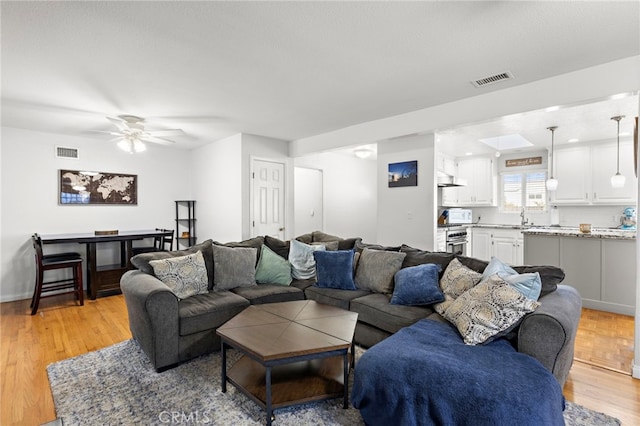 living room featuring ceiling fan, visible vents, baseboards, and light wood-style flooring