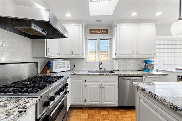 kitchen with light stone countertops, a sink, white cabinets, appliances with stainless steel finishes, and wall chimney exhaust hood