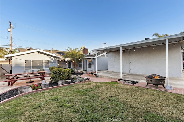 rear view of property featuring stucco siding, a patio, a lawn, and an outdoor fire pit