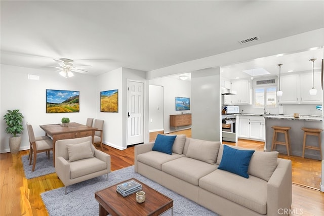 living area featuring light wood-type flooring, baseboards, visible vents, and ceiling fan