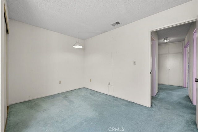 spare room featuring light carpet, visible vents, and a textured ceiling