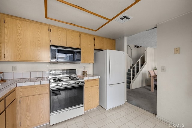 kitchen featuring range with gas stovetop, tile counters, visible vents, freestanding refrigerator, and black microwave