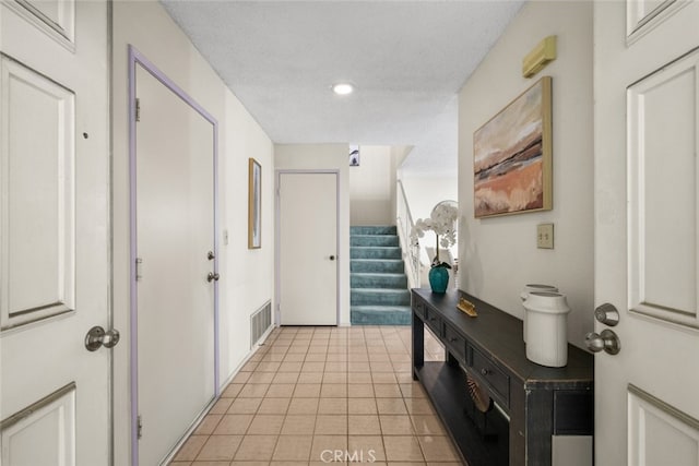 interior space featuring a textured ceiling, light tile patterned floors, stairway, and visible vents