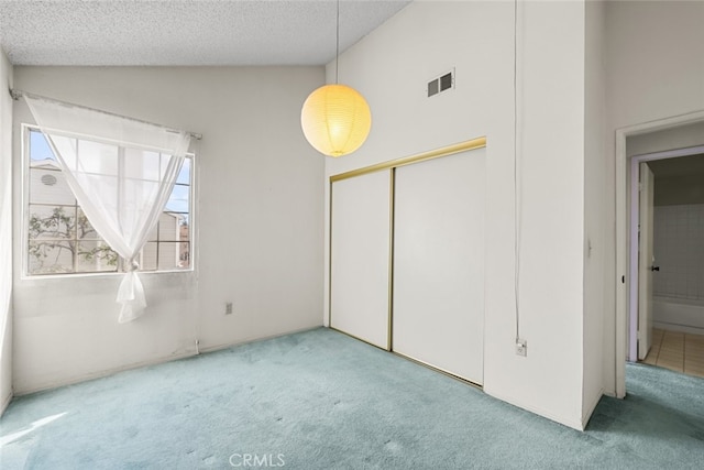 unfurnished bedroom with visible vents, light colored carpet, vaulted ceiling, a textured ceiling, and a closet