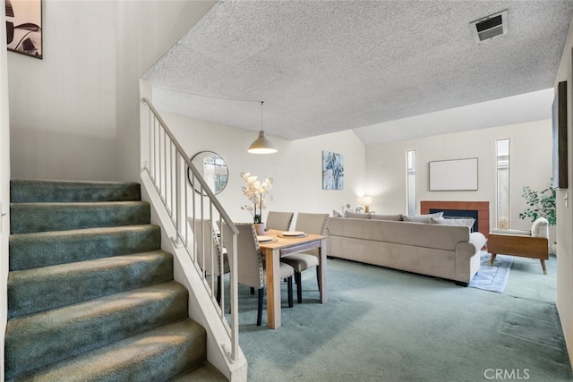 interior space featuring lofted ceiling, visible vents, a tiled fireplace, carpet flooring, and a textured ceiling