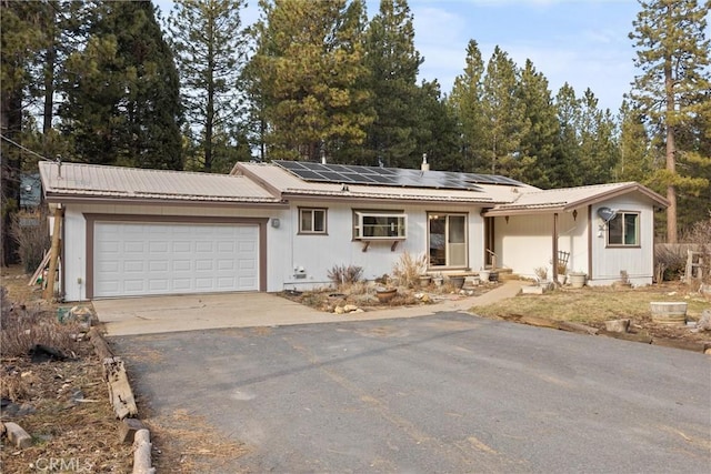 single story home with a garage, metal roof, driveway, and roof mounted solar panels