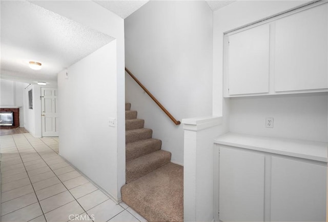 stairway with a brick fireplace and tile patterned floors