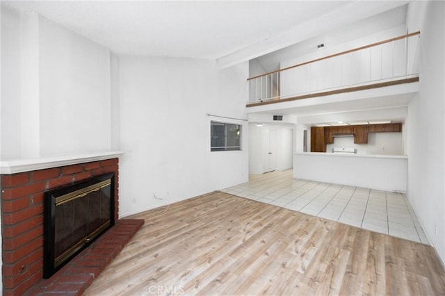 unfurnished living room featuring visible vents, light wood-style floors, beamed ceiling, a brick fireplace, and high vaulted ceiling