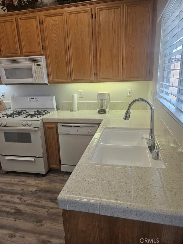 kitchen featuring brown cabinetry, white appliances, dark wood-type flooring, and a sink