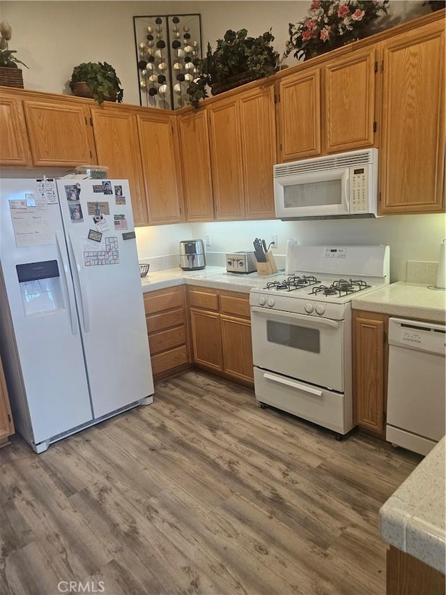 kitchen featuring light countertops, white appliances, wood finished floors, and brown cabinets