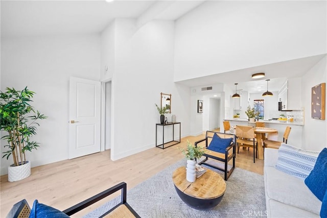 living room with visible vents, a high ceiling, light wood-style flooring, and baseboards