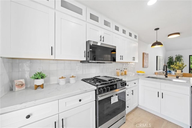 kitchen featuring glass insert cabinets, stainless steel appliances, white cabinetry, pendant lighting, and a sink