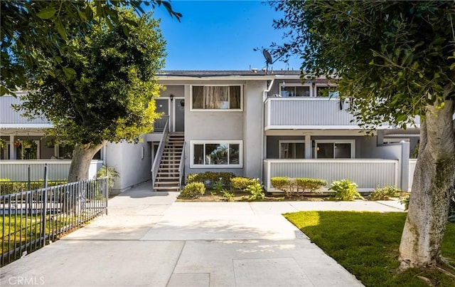 view of property featuring stairway, fence, and stucco siding